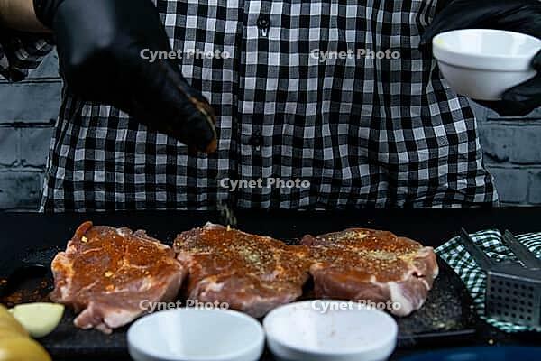 A chef in black gloves with red pepper blows up a raw tenderoin. Fresh raw pork tongs on a wooden cutting board. Close up [IBR125462131]