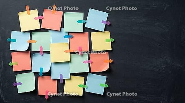 Blank colorful sticky notes with small arrow markers pointing in different directions on charcoal slate wall, indecision concept, studio shot, AI generated [IBR125472251]