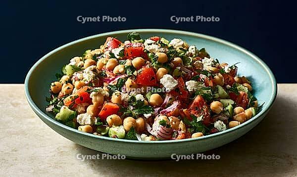 Fresh chickpea salad with tomatoes, cucumber, feta, and parsley. Vibrant bowl on wooden surface. Dark blue background adds contrast, AI generated [IBR125472252]