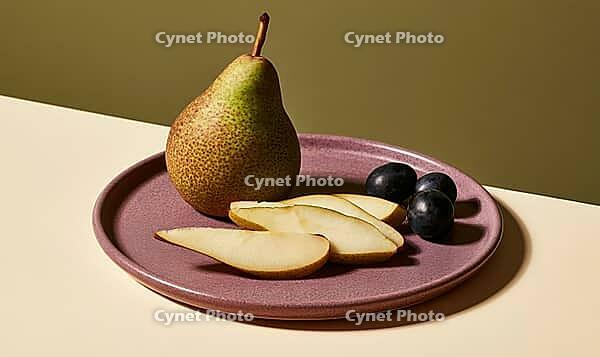 Single pear and sliced fruit on purple plate. Three black grapes beside pear. Warm lighting highlights textures, AI generated [IBR125472253]