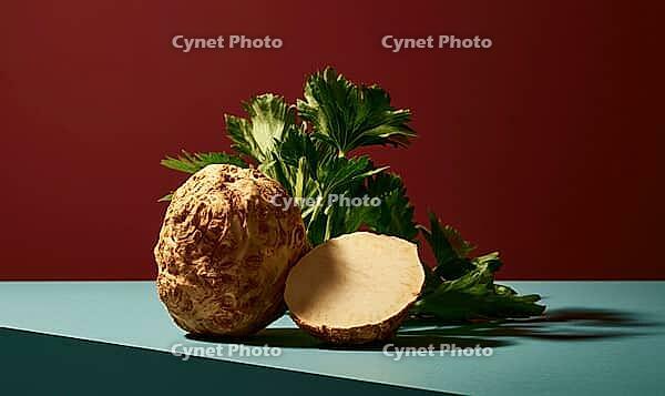 Celeriac root, cut in half, with green leafy tops on a teal surface against a deep red background, AI generated [IBR125472258]