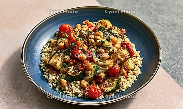 Blue plate holds quinoa, chickpeas, zucchini, and cherry tomatoes. Meal is fresh, colorful, and healthy. Plate rests on light pink and gray surface, AI generated [IBR125472262]