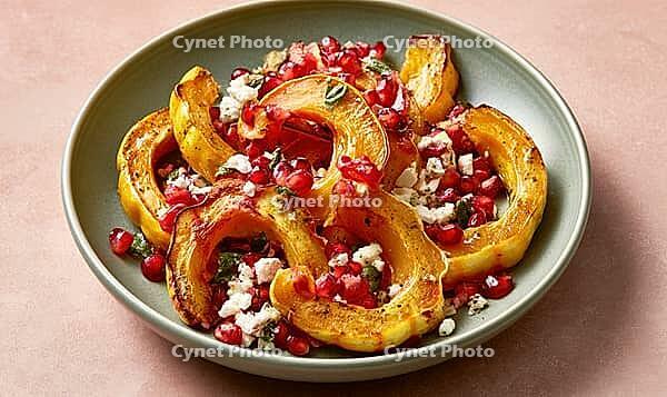 Roasted squash slices topped with pomegranate seeds and feta cheese on a green plate, AI generated [IBR125472266]