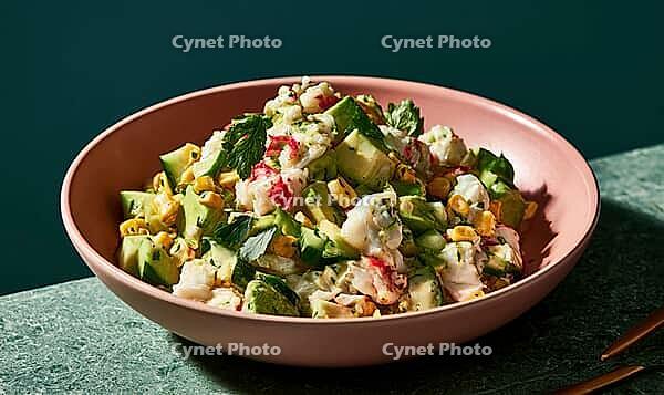 Fresh seafood salad in pink bowl on green surface. Mixed with diced cucumber, corn, and herbs. Light dressing coats ingredients evenly, AI generated [IBR125472270]