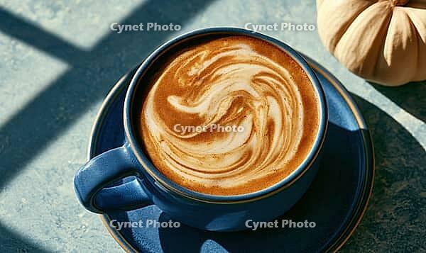 Cup of coffee with latte art on blue saucer. Sunlight casts shadows across textured surface. Pumpkin sits beside cup, suggesting autumn theme, AI generated [IBR125472286]
