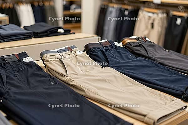 Folded trousers on a retail display table showcase menswear fashion garments and organized textile merchandising in a contemporary department store, precisely tailored cotton chinos and casual slacks arranged in alternating palettes of navy blue, warm kha [IBR125472292]