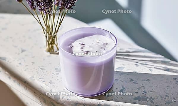 Lavender candle in glass jar on speckled surface. Bouquet of lavender flowers beside it. Natural light casts soft shadows, AI generated [IBR125472294]