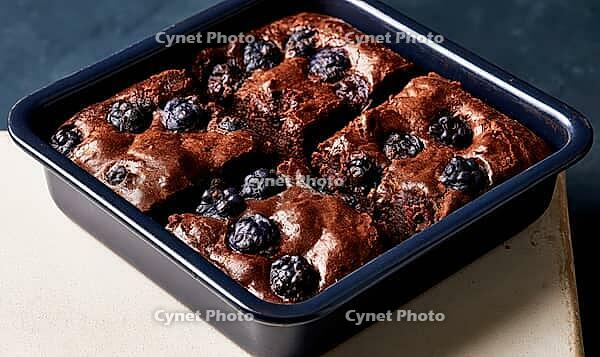 Freshly baked chocolate brownies with blueberries in pan. Rich, moist texture with visible berries on top. Dark pan sits on light countertop surface, AI generated [IBR125472307]