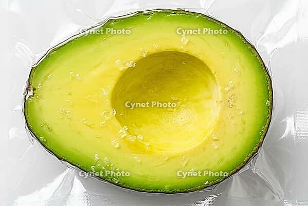 Vacuum sealed avocado half with sea salt crystals in transparent plastic packaging for food preservation, sous vide culinary preparation and freshness, high pressure processing technology shields perishable organic fruit flesh against rapid oxidation, the [IBR125472337]