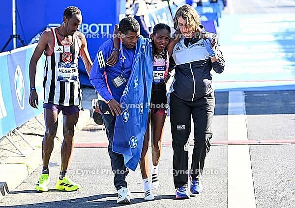 27 September 2026, Athletics: BMW Berlin Marathon 2026, from left: Tigst Assefa (ETH 2:11:04) crosses the finish line, exhausted, and is supported by a team at the 2026 BMW BERLIN MARATHON [IBR113453171]