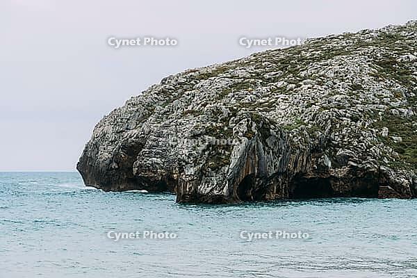 Sandy Cuevas del Mar beach with turquoise ocean water and waves breaking near large rock formations and green cliffs [IBR125492349]