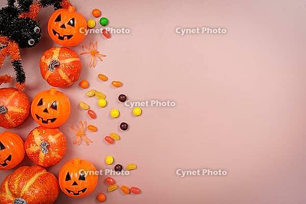 Top view of jack o lantern pumpkins, colorful candies, and toy spiders arranged on a pink background with empty space for text [IBR125492358]