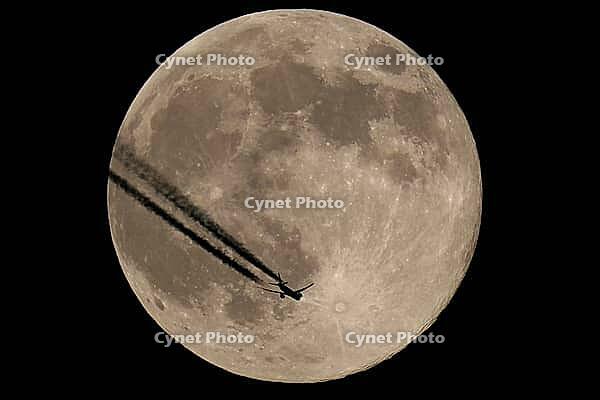 The moon and a plane in the night sky. The plane flies over the moon, against a black background [IBR125492364]