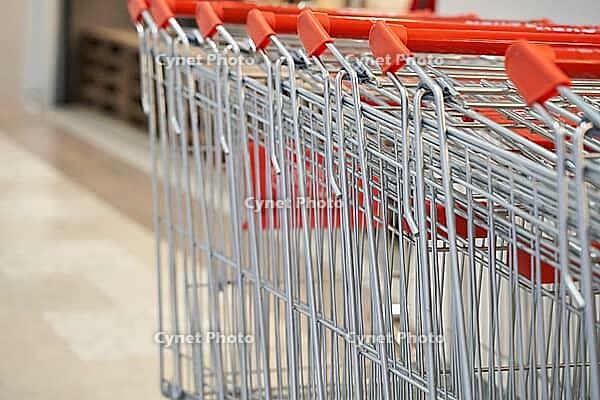 Shopping cart embedded in metal row with red handles at supermarket entrance on tile floor near checkout area displayed Organized retail access for customers [IBR125492377]