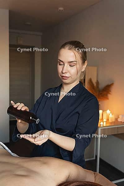 Professional masseuse pouring essential oil into hand, preparing for a calming body massage and wellness therapy session [IBR125492391]