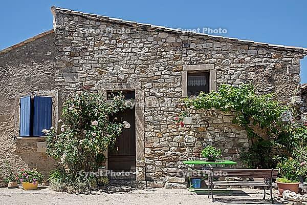 Rustic stone house with blue shutters surrounded by flowers and climbing plants, a table with chairs in front of it, Aurel, Provence, France [IBR125492397]