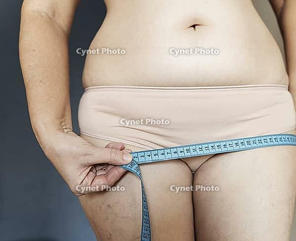 Woman measuring hips with tape measure, tracking weight loss and body transformation for health, fitness, and wellness goals [IBR125492411]