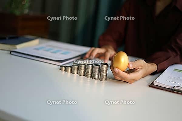 Rising stack of coins on table and golden eggs on businessman hand metaphor for financial planning and investment return [IBR125492413]
