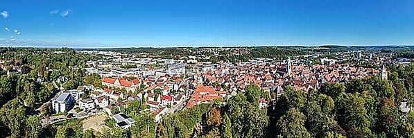 Impressive bird's-eye view of Biberach an der Riß. The photo shows the historic old town with its characteristic red roofs, traditional half-timbered houses and distinctive church towers. Nestled in a hilly, green wooded landscape, the urban area stretche [IBR125501639]