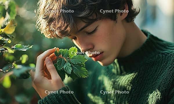 Closeup portrait of a man with warm brown hair, holding a bunch of soft green leaves, AI generated [IBR125502135]