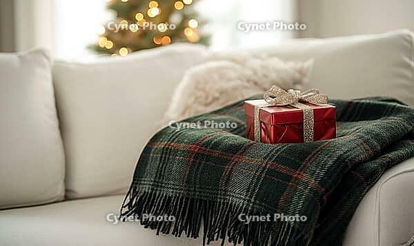 Cozy winter scene with a dark green plaid blanket folded on a white sofa, a small red gift box nearby, soft ambient light enhancing textures, AI generated [IBR125502147]
