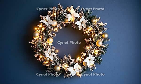 Elegant round holiday wreath with white and gold decorations against a matte dark blue wall, tiny warm lights on the wreath adding a cozy glow, AI generated [IBR125502149]