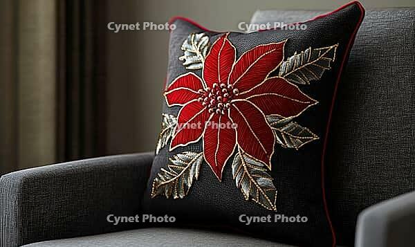 Dark chocolate pillow with bright red poinsettia and gold stitching, on a warm gray armchair, AI generated [IBR125502178]