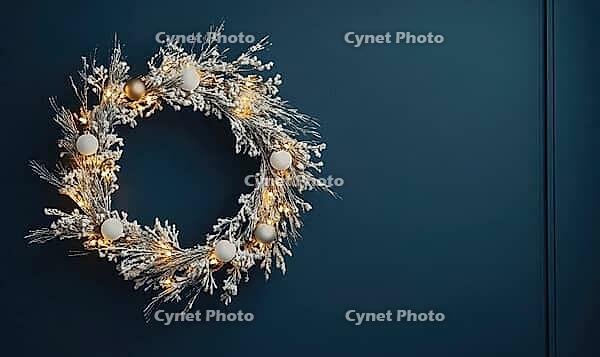 Elegant round holiday wreath with white and gold decorations against a matte dark blue wall, tiny warm lights on the wreath adding a cozy glow, AI generated [IBR125502190]