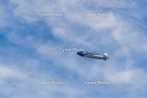 A blue airship with advertising inscription floats in front of a light blue, cloudy sky, Zeppelin, ZF, Konstanz am Lake Constance, Baden-Württemberg, Germany [IBR125521082]