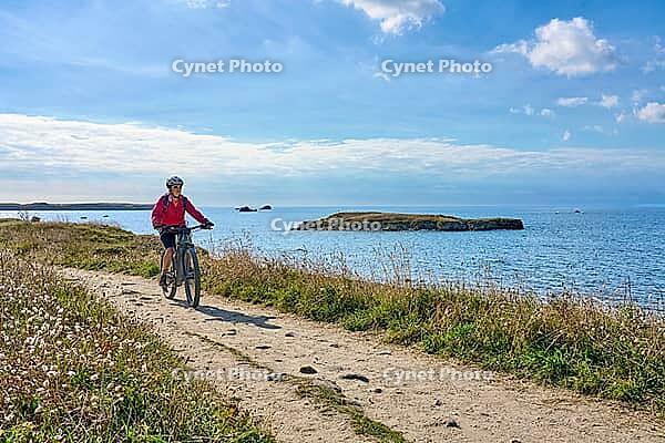 Active senior woman cycling with electric mountain bike along the wild atlantic coast of Quiberon Peninsula, Brittany, France [IBR125521103]