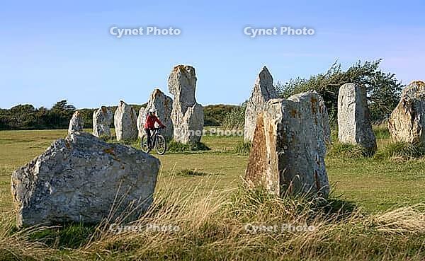 Woman cycling between the neolithic menhirs of Camaret sur mer in Brittany, France [IBR125521118]