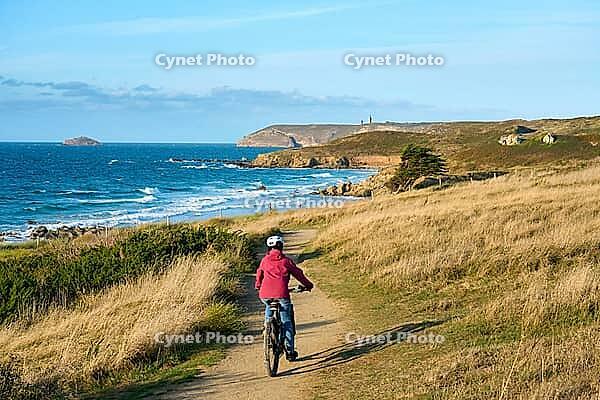 Active senior woman cycling with her electric mountain bike along the wild atlantic coast of Finisterre at Cape Frehel, Brittany, France [IBR125521119]
