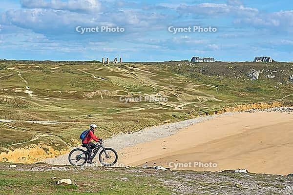 Active senior woman cycling with her electric mountain bike along the wild coast of Finisterre in southern Brittany next to Camaret-sur-Mer, France [IBR125521121]