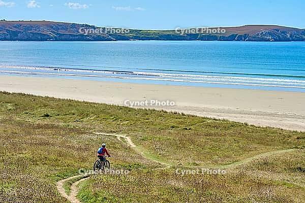 Active senior woman cycling with her electric mountain bike along the wild coast of Finisterre in southern Brittany next to Camaret-sur-Mer, France [IBR125521123]
