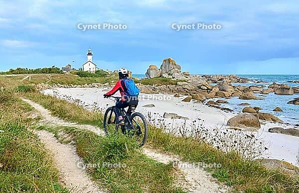 Nice senior woman cycling with her electric mountain bike at the rocky rose granite coast at Meneham site in Kerouarn, Brittany, FranceKerouarn [IBR125521130]