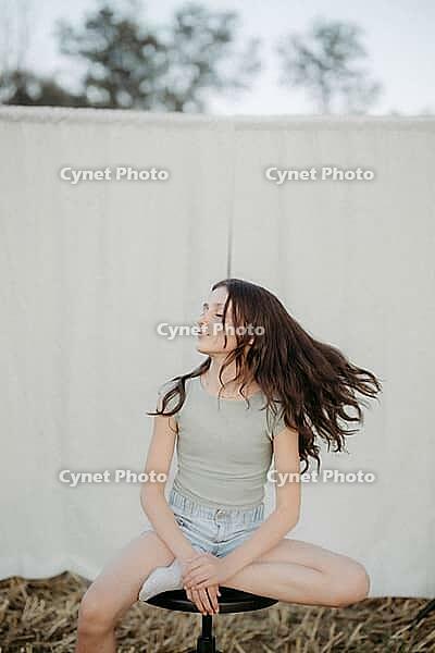Brown-haired girl, 11, sitting on a stool in a cornfield against a beige background [IBR125521132]