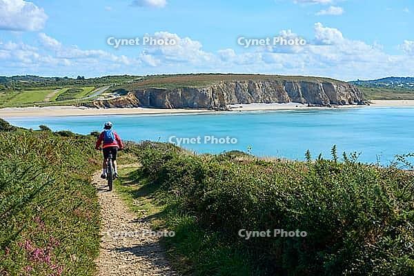 Active senior woman cycling with her electric mountain bike along the wild coast of Finisterre in southern Brittany next to Camaret-sur-Mer, France [IBR125521133]