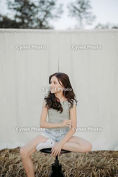 Brown-haired girl, 11, sitting on a stool in a cornfield against a beige background [IBR125521146]