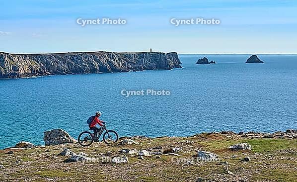 Active senior woman cycling with her electric mountain bike along the wild coast of Finisterre in southern Brittany next to Camaret-sur-Mer, France [IBR125521148]