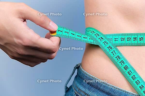 A woman measures her waist with a tape measure. Diet and body weight control concept, close-up, toned. A girl in jeans takes measurements of her figure and weight loss [IBR125527050]