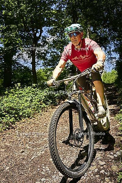 Mountain biker riding a root trail in the forest. Frontal view. Zurich Oberland, Switzerland [IBR125527061]
