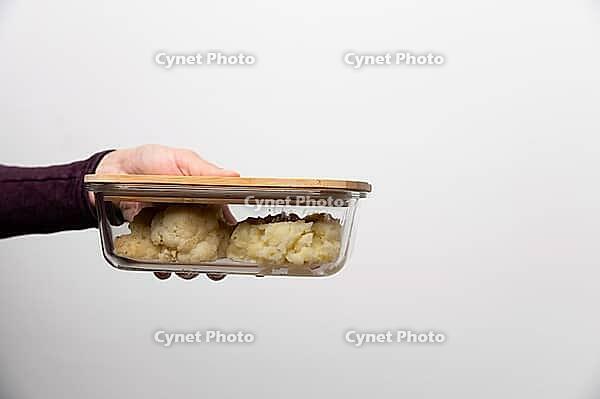Close-up of woman taking out container with cauliflower. Hand shows glass container with lunch food brought to work [IBR125527067]