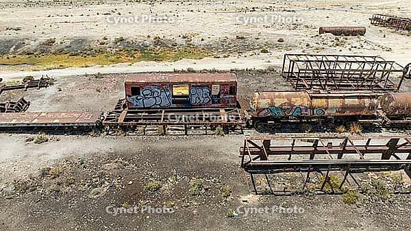 Train Cemetery featuring rusted locomotive skeletons and abandoned railway carriages scattered across the arid desert landscape. Aerial view [IBR125536413]