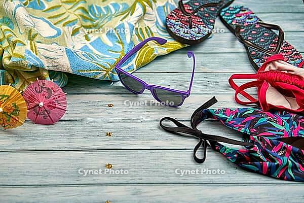 Swimwear, sunglasses, flip flops and beach towel with a tropical print on a wooden table [IBR125536420]