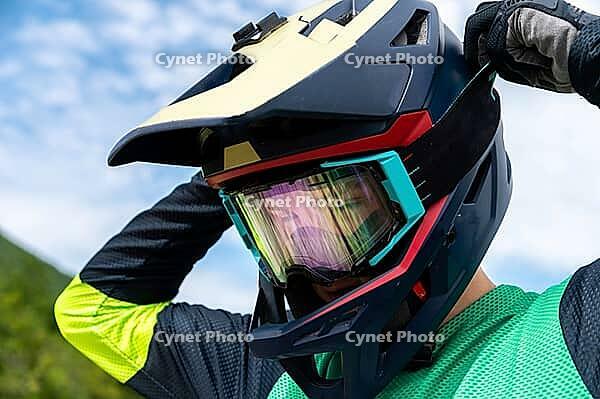 Guy adjusting motorcycle motocross helmet with goggles, close-up shot of relaxing while riding bike or dirt bike [IBR125536431]