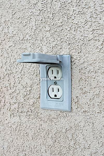 Electric outdoor outlet with lid in a beige stucco wall [IBR125536439]