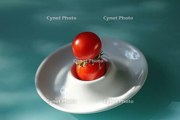 Two shiny red tomatoes grow on top of each other in a white bowl on a turquoise surface, Horn Bad Meinberg [IBR125536443]