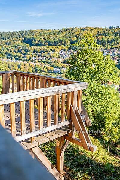 A wooden viewpoint offers a wide view of green hills and a village under a blue sky, Calw City Garden, Black Forest, Germany [IBR125536475]