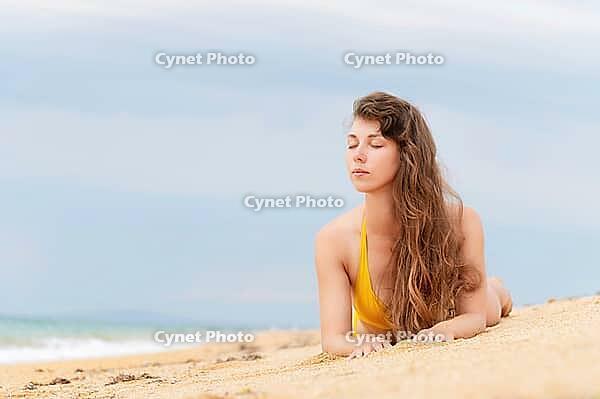 Beautiful woman with perfect body lies on sandy beach, wearing yellow bikini, sunbathing at beach resort, enjoying summer vacation [IBR125536482]