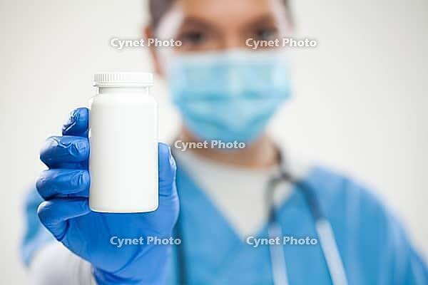 Women UK NHS general professional doctor, laundry, protective face mask and gloves, holding white empty bottle pills, blank no label container suitable for adding custom text, selective focus [IBR125557531]